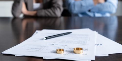 Divorce papers with wedding rings and couple in background at a table.