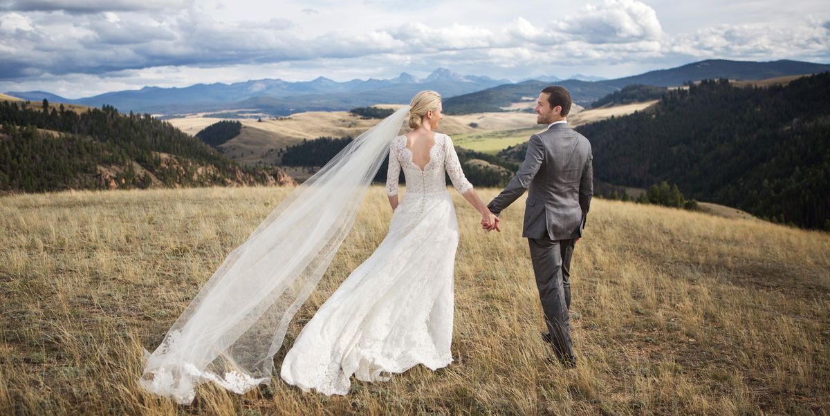 Bride and groom holding hands on a scenic mountain landscape.