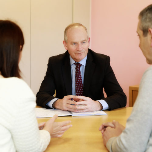 Man in a suit speaking with a couple at a desk in a meeting room.