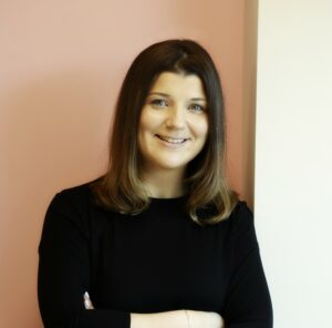 Smiling woman in black top against a peach wall background.