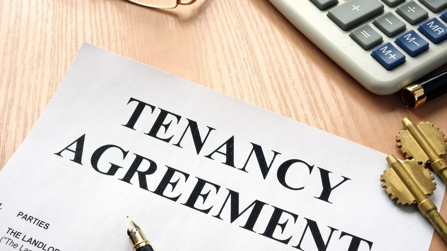 Tenancy agreement form with pen, calculator, and keys on wooden desk.