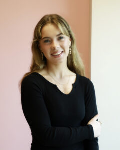 Smiling woman in black top with pink background.