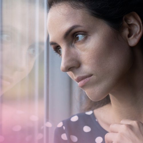Woman gazing out of a window, deep in thought, wearing a polka dot dress.