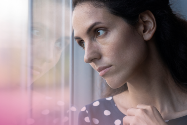 Woman gazing out of a window, deep in thought, wearing a polka dot dress.