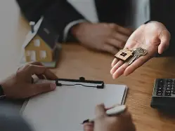Estate agent handing house keys to client at desk with contract.