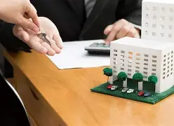 Person handing over keys next to architectural model, symbolising real estate transaction.