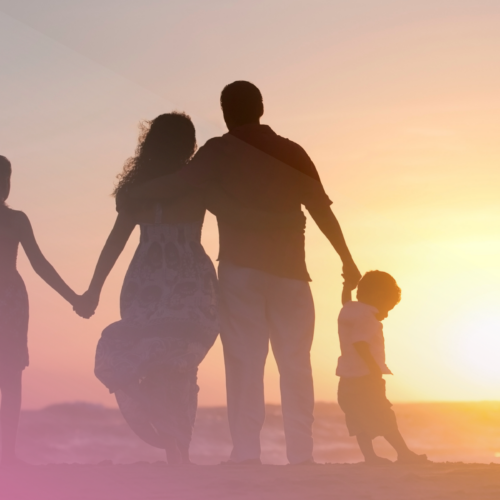Family enjoying a beach sunset, holding hands with pink sky and warm glow.
