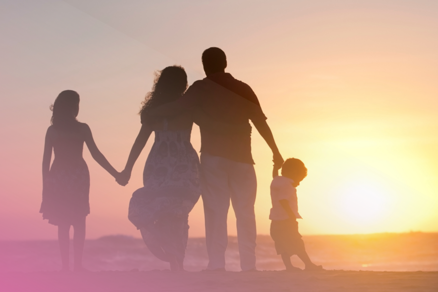 Family enjoying a beach sunset, holding hands with pink sky and warm glow.