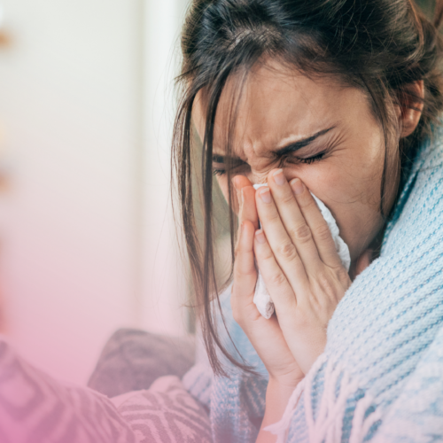 Sick Woman sneezing indoors, wrapped in a cosy blue blanket.