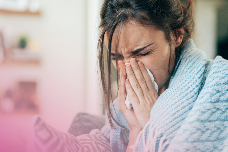 Sick Woman sneezing indoors, wrapped in a cosy blue blanket.