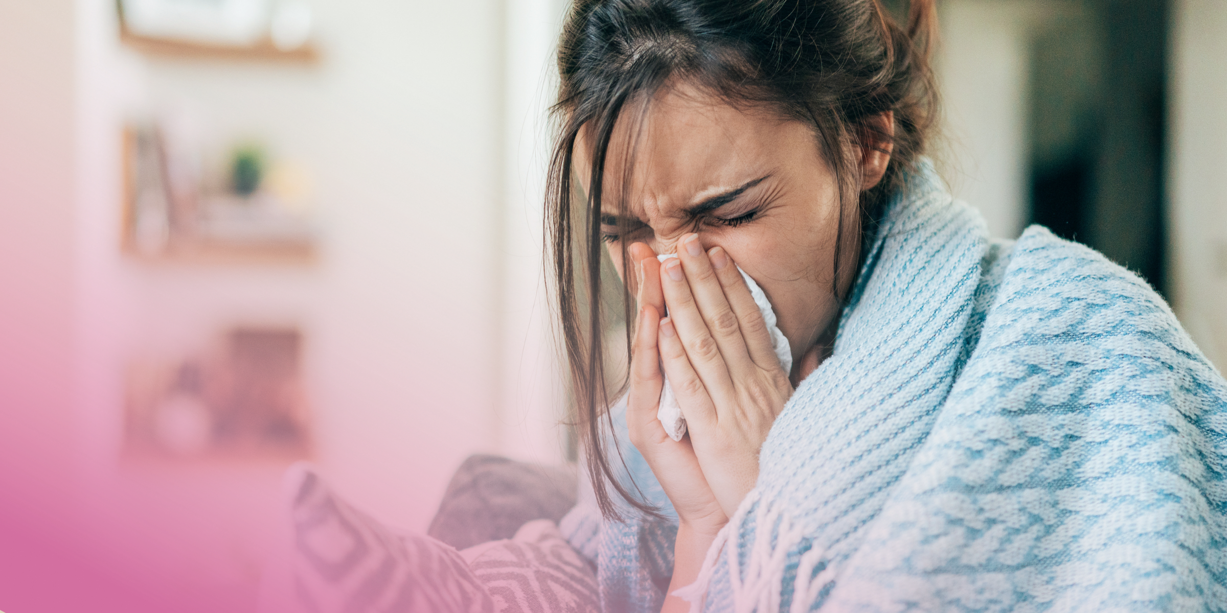 Sick Woman sneezing indoors, wrapped in a cosy blue blanket.