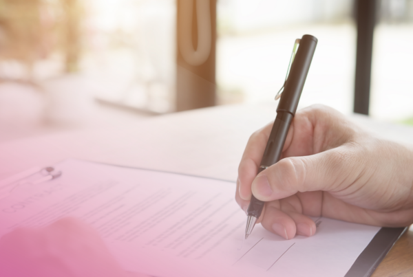 Close-up of a hand signing a contract on a clipboard with a pen.