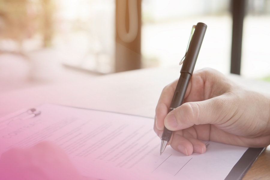 Close-up of a hand signing a contract on a clipboard with a pen.