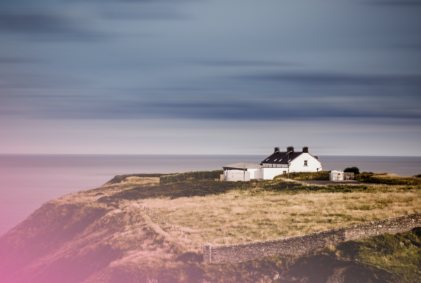 White cottage on a serene cliffside overlooking the sea under a cloudy sky.