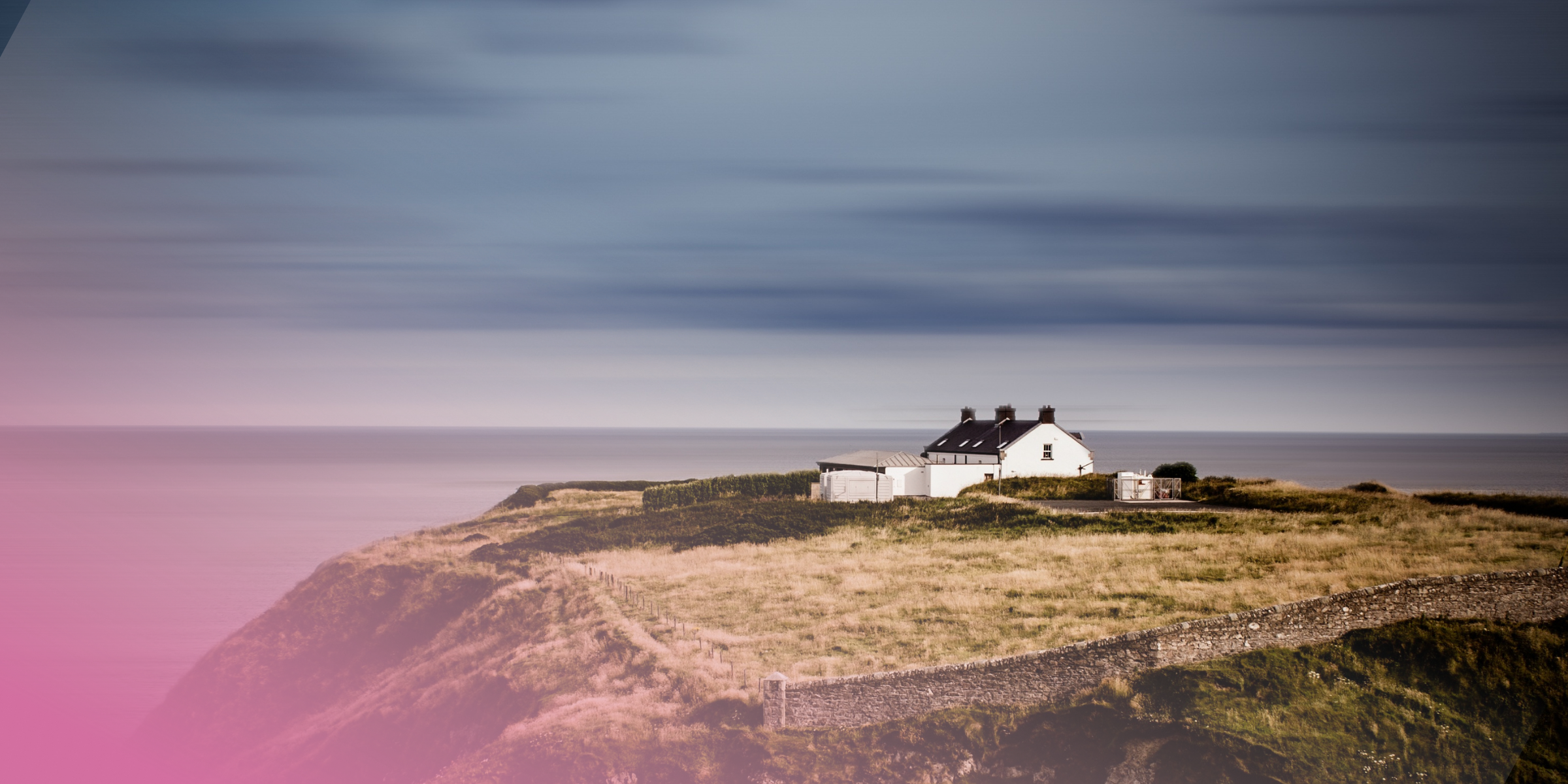 White cottage on a serene cliffside overlooking the sea under a cloudy sky.