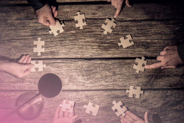 Hands arranging jigsaw puzzle pieces on a wooden table.