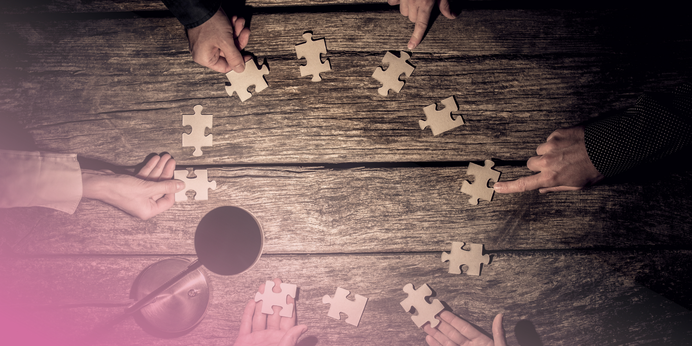 Hands arranging jigsaw puzzle pieces on a wooden table.