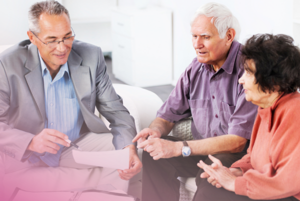 Elderly couple in discussion with advisor, reviewing documents on sofa.
