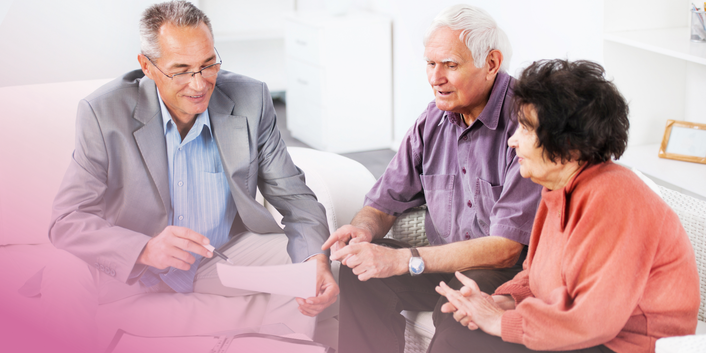 Elderly couple in discussion with advisor, reviewing documents on sofa.