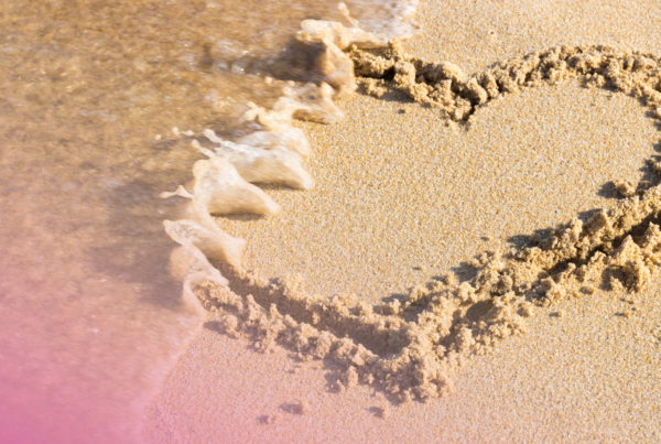 Heart shape drawn in sand as a wave washes over, symbolising fleeting moments by the seaside.