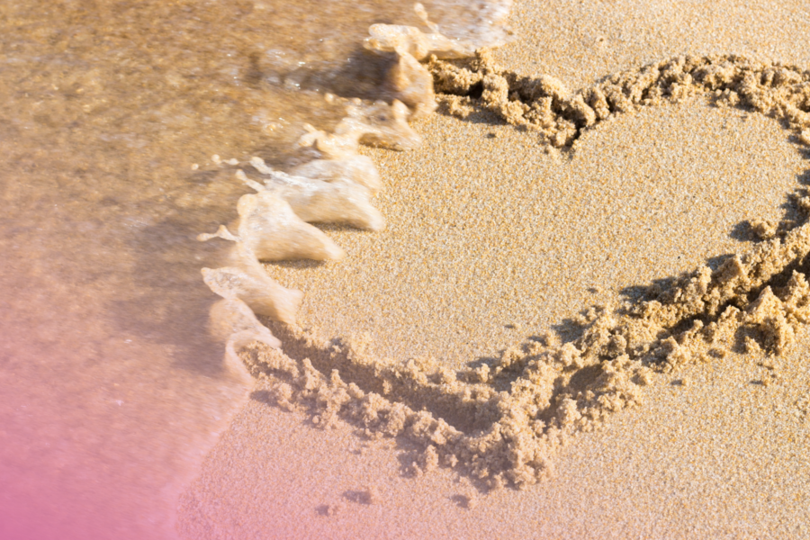 Heart shape drawn in sand as a wave washes over, symbolising fleeting moments by the seaside.