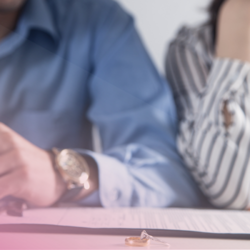Couple signing divorce papers with wedding rings on table.