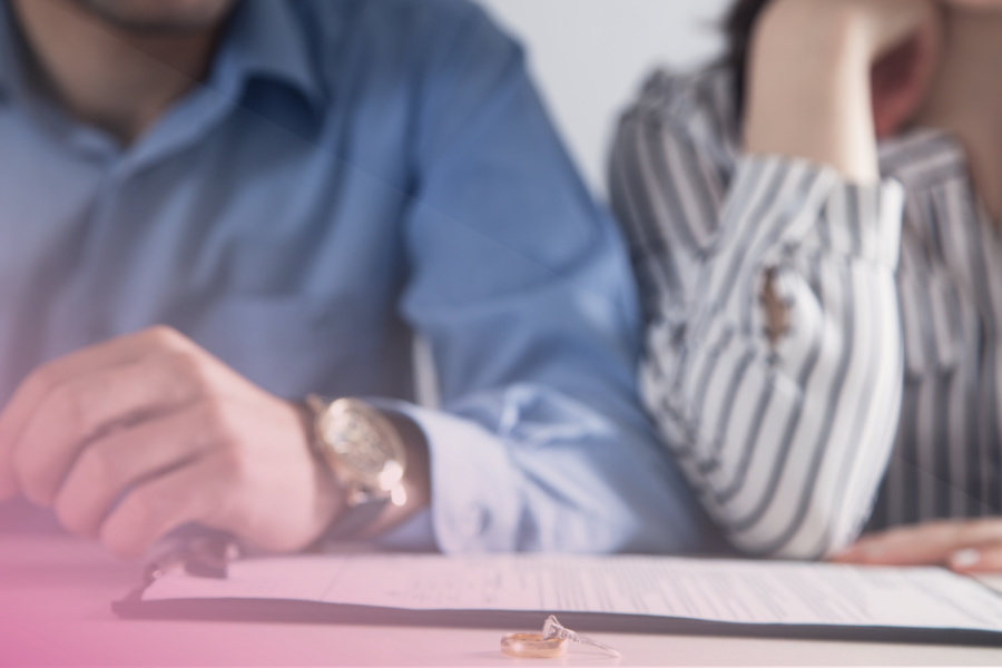 Couple signing divorce papers with wedding rings on table.