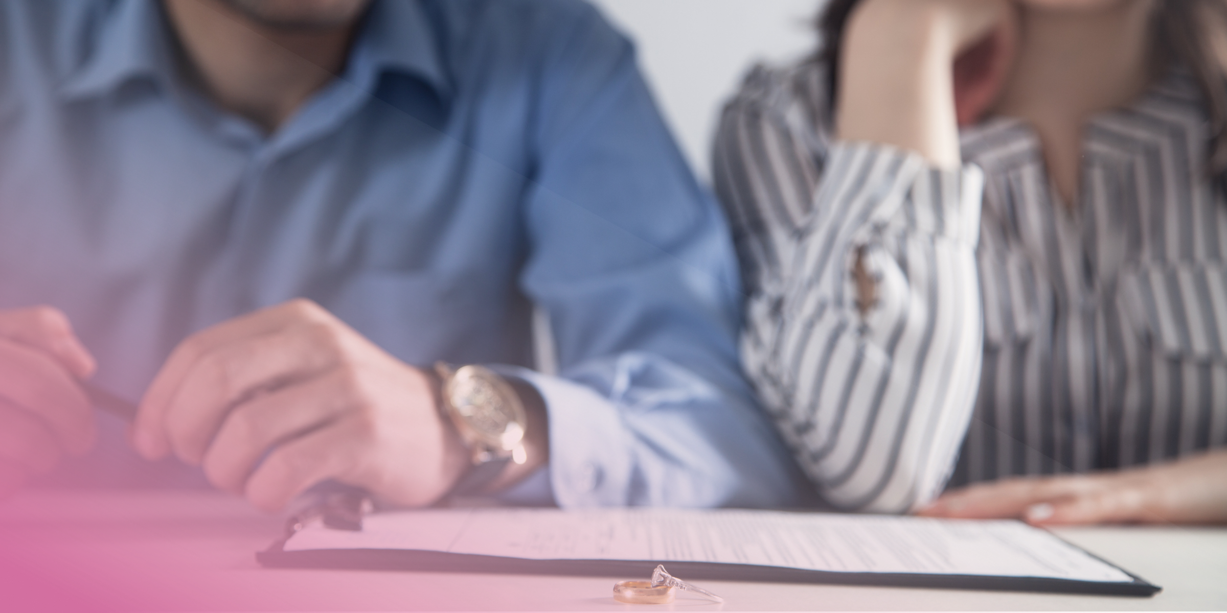 Couple signing divorce papers with wedding rings on table.