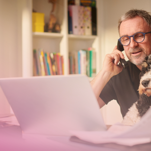Man working from home with dog, using laptop and phone.