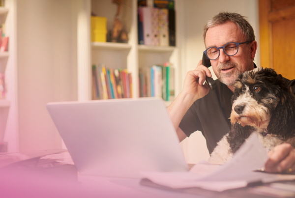 Man working from home with dog, using laptop and phone.