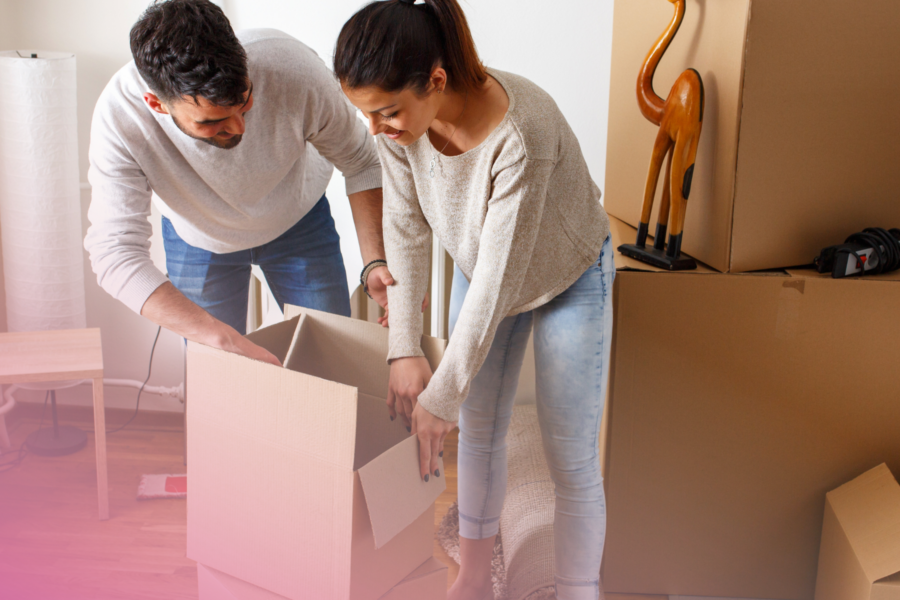 Couple unpacking boxes in new home, surrounded by cardboard packages.