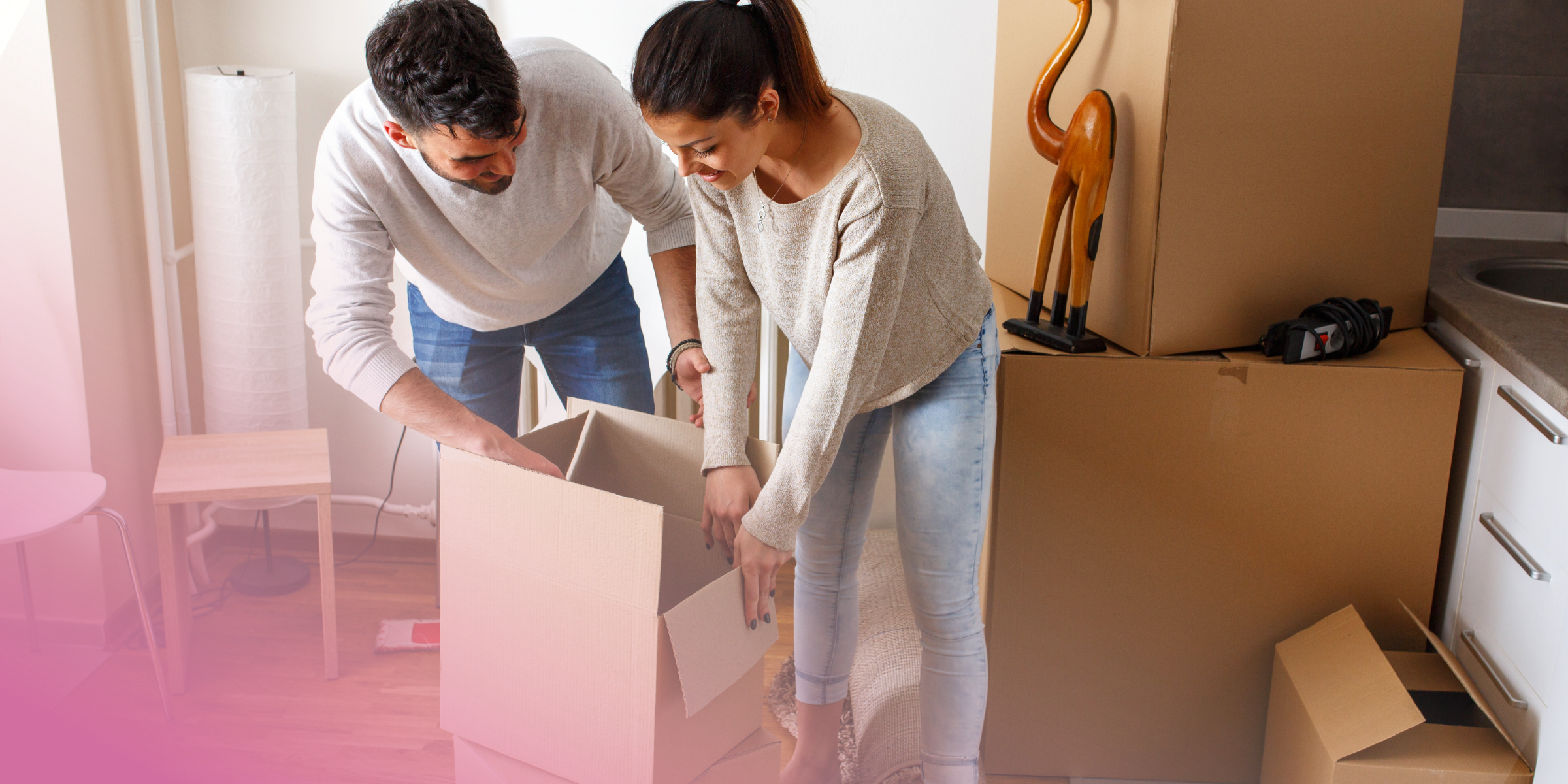 Couple unpacking boxes in new home, surrounded by cardboard packages.