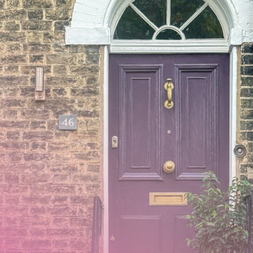 Purple front door of a brick house with brass fixtures and arched window.