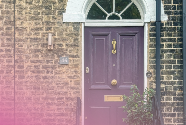 Purple front door of a brick house with brass fixtures and arched window.