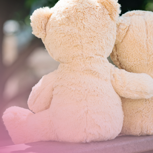 Two teddy bears sitting together on a bench with a soft pink glow.