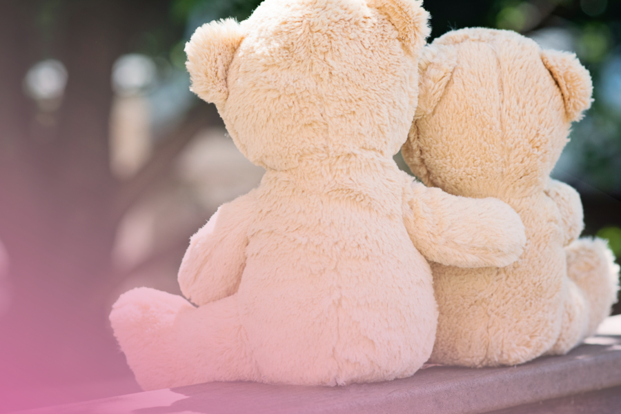 Two teddy bears sitting together on a bench with a soft pink glow.